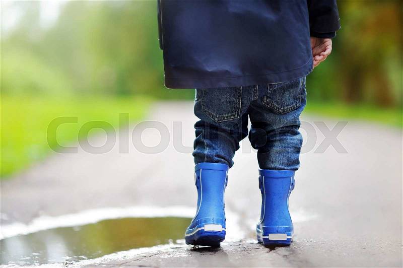 Toddler wearing rain boots standing near a puddle on the summer or autumn day, stock photo