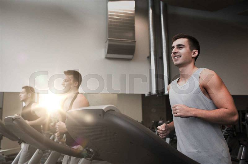 Sport, fitness, lifestyle, technology and people concept - smiling men exercising on treadmill in gym, stock photo