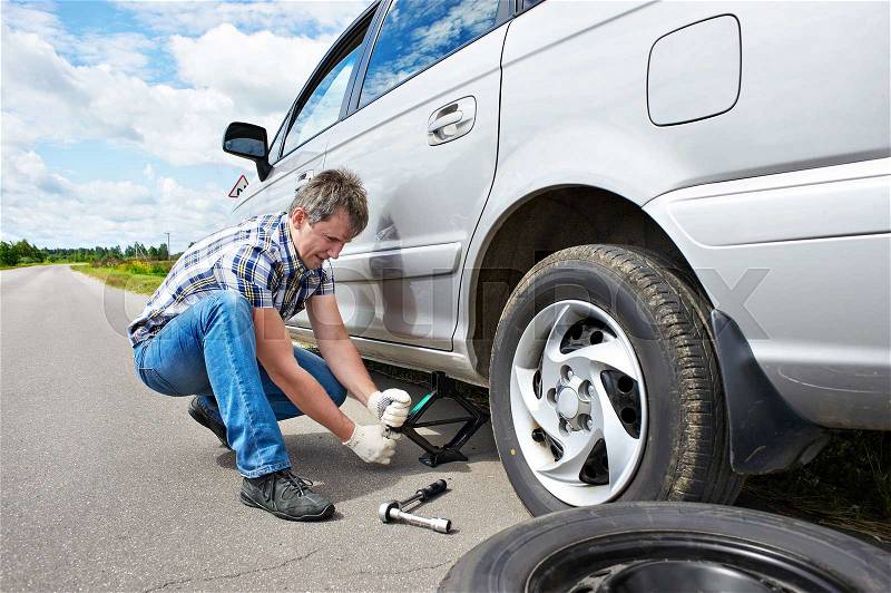 Man changing a spare tire of car on road, stock photo