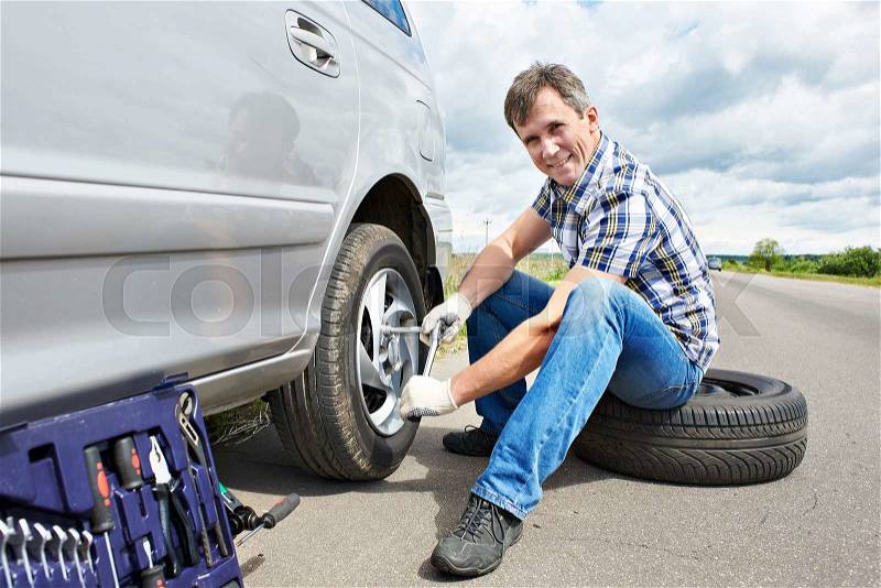 Man with jack changing a spare tire of car on road, stock photo