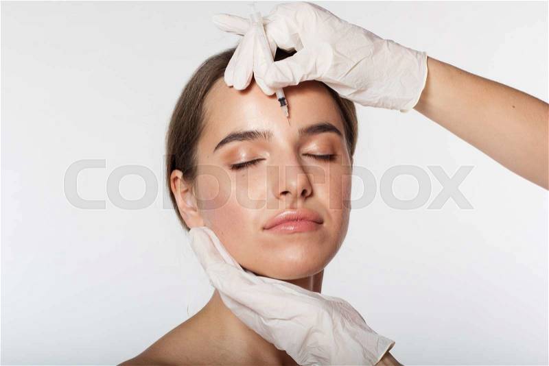 Young woman getting beauty injection by doctor in white gloves isolated on white, stock photo