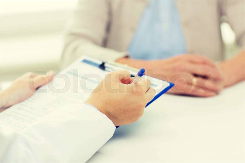 Medicine, age, health care and people concept - close up of senior woman and doctor hands with clipboard meeting in medical office, stock photo