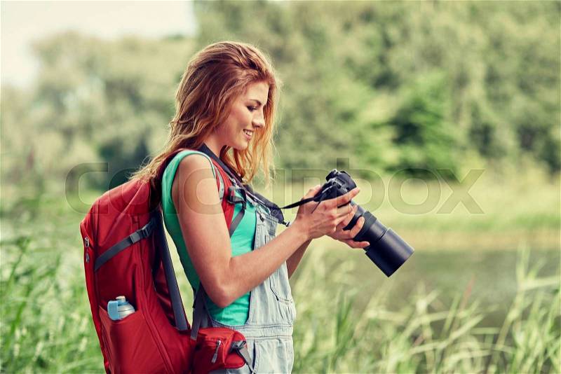 Adventure, travel, tourism, hike and people concept - happy young woman with backpack and camera photographing outdoors, stock photo