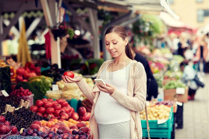 Sale, shopping, food, pregnancy and people concept - happy pregnant woman with smartphone choosing vegetables at street market, stock photo