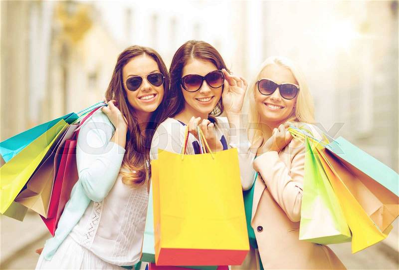 Shopping, sale, happy people and tourism concept - three beautiful girls in sunglasses with shopping bags in ctiy, stock photo