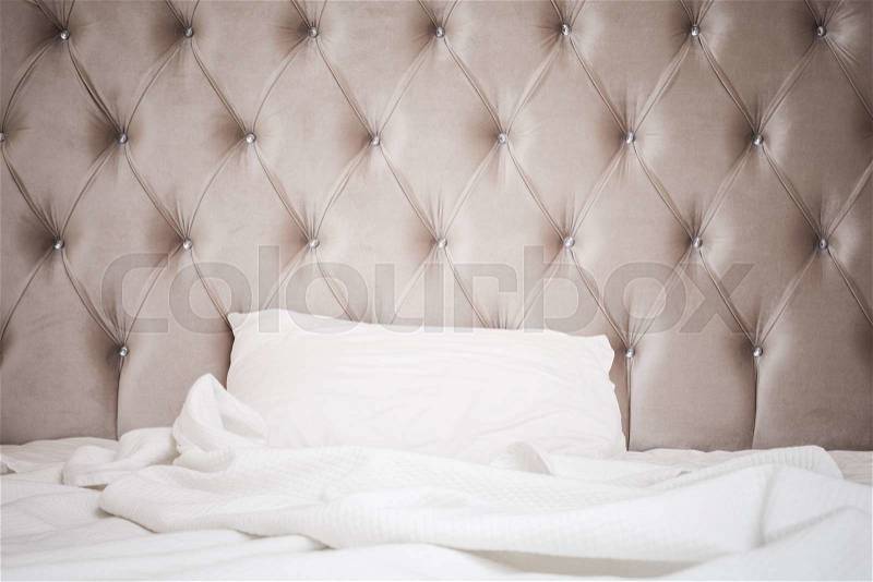 Luxury empty bedroom interior fragment, soft pink headboard, white bedding sheet and pillow lay on wide empty bed, stock photo