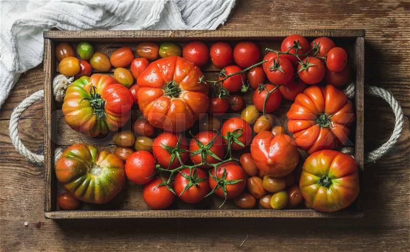 Colorful assortment of heirloom, bunch and cherry tomatoes in wooden tray over rustic wooden background, top view, horizontal composition, stock photo