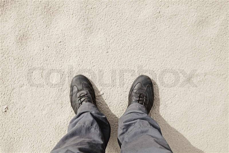 Male feet in leather shoes stand on white wet sand ground, first person view, stock photo