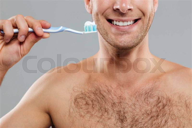Cheerful young man cleaning teeth with toothbrush and toothpaste and smiling, stock photo