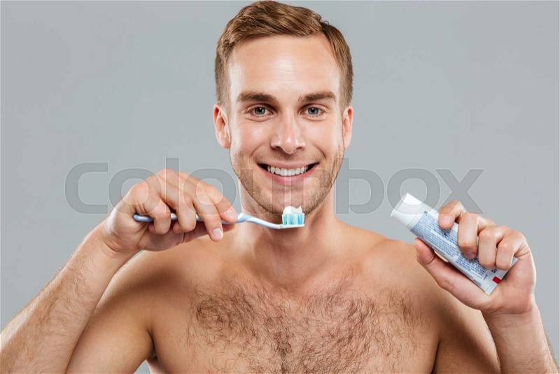 Happy naked young man cleaning teeth with toothbrush and toothpaste, stock photo