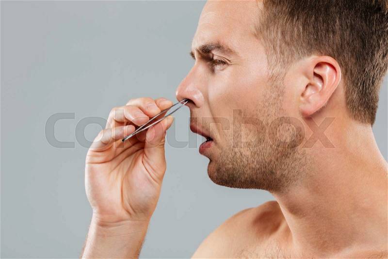 Side view of a man removing nose hair with tweezers isolated on the gray background, stock photo