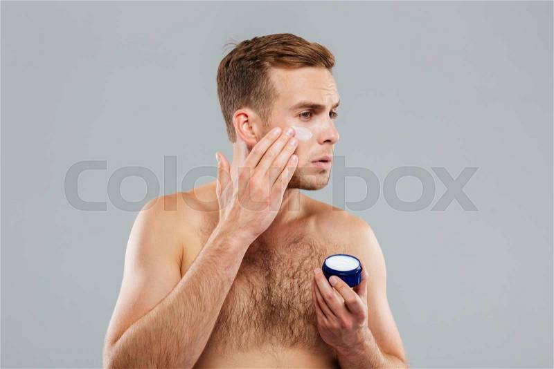 Man putting on cream lotion on face isolated on the gray background, stock photo