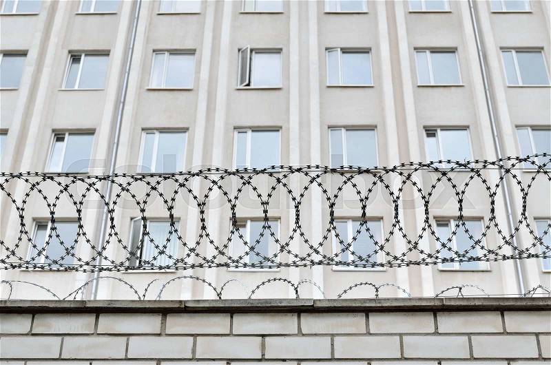 Gray building is fenced with barbed wire. Symbol of dictatorial and authoritarian regime. Limitation limitation of freedom and human rights, stock photo