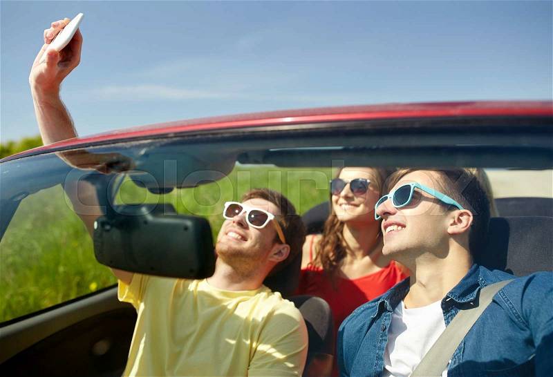 Leisure, road trip, travel and people concept - happy friends driving in cabriolet taking selfie by smartphone outdoors, stock photo