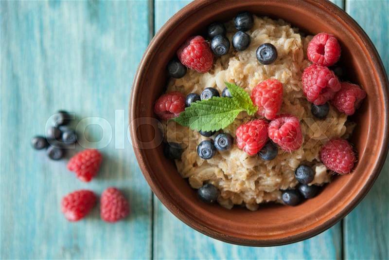 Food background with plate of oat flakes, raspberries and blueberries on blue vintage board. Eating or vegetarian concept, stock photo