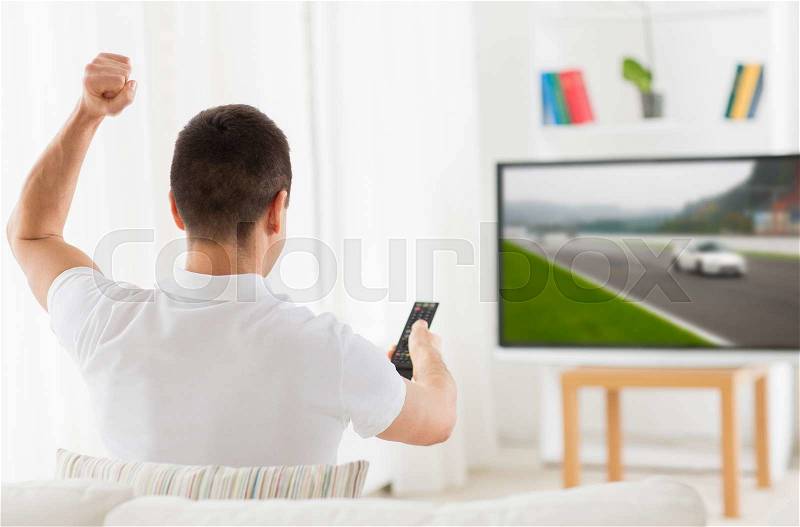 Leisure, technology, motorsports, sport and people concept - man with remote control watching car racing on tv at home, stock photo