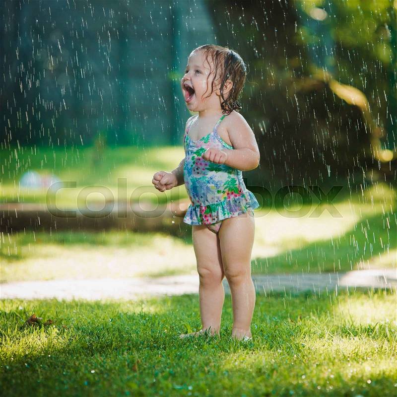The little baby girl playing with garden sprinkler. Summer outdoor water fun and green grass, stock photo