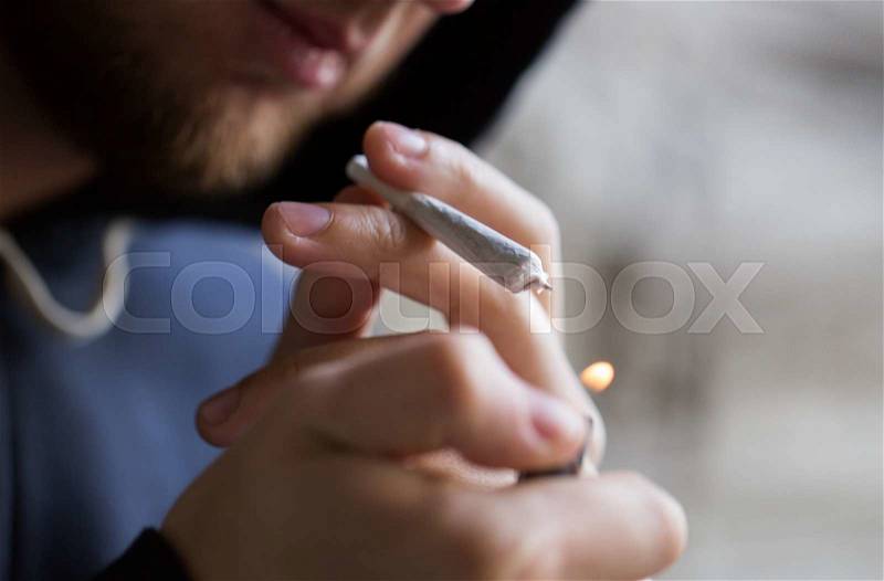 Drug use, substance abuse, addiction, people and smoking concept - close up of addict lighting up marijuana joint with lighter, stock photo
