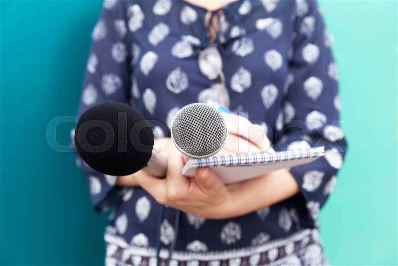 Female journalist or reporter at press conference, taking notes, holding microphones, stock photo