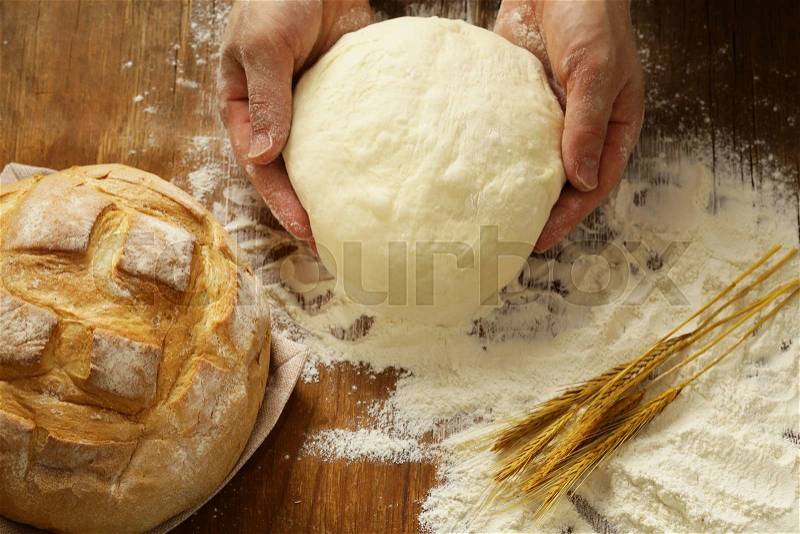 Chef hands with dough and homemade natural organic bread and flour on a wooden background, stock photo