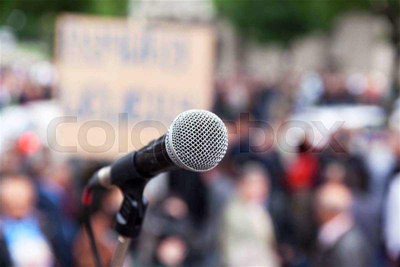 Microphone in focus against blurred crowd. Political rally, stock photo