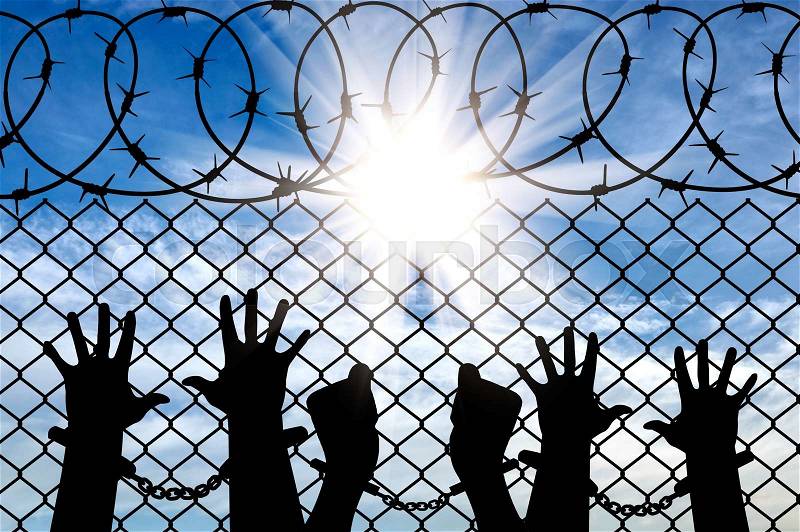Silhouette of a crowd of hands in handcuffs near the fence with barbed wire, stock photo