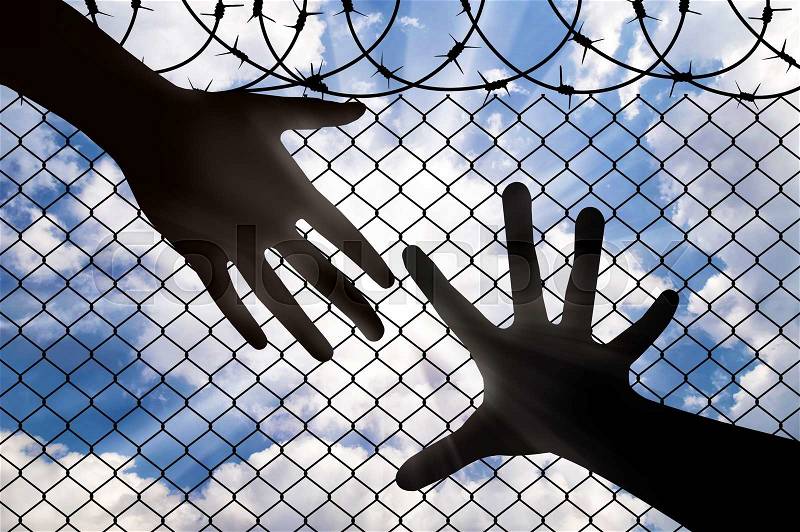 Assistance to refugees concept. A Helping Hand, reaches for the hand of a refugee, against the fence of barbed wire, stock photo