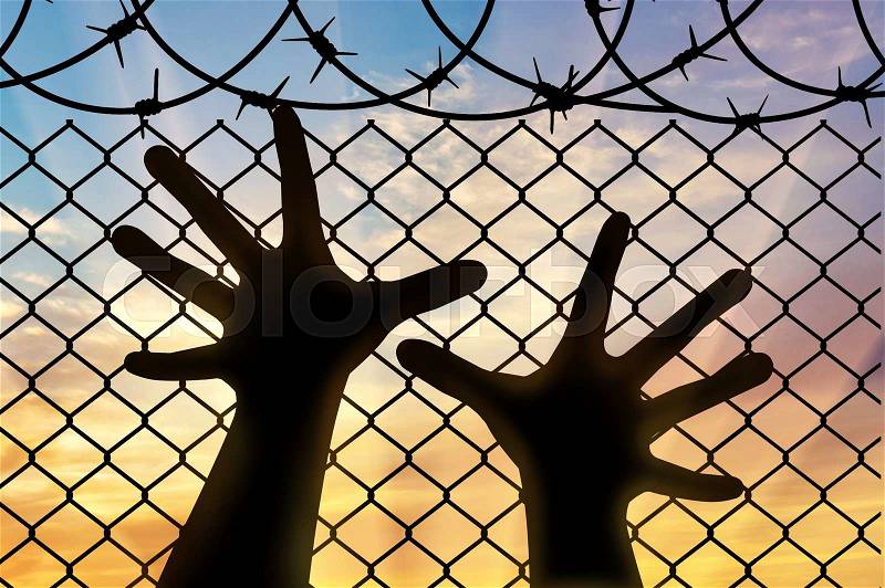 Refugees concept. Silhouette refugee hands near the barbed wire fence, stock photo