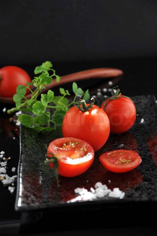 Fresh red tomato on tray with sea salt on black background, stock photo