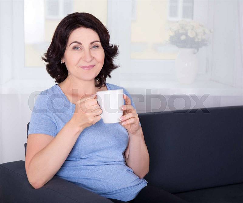 Happy mature woman drinking coffee at home, stock photo