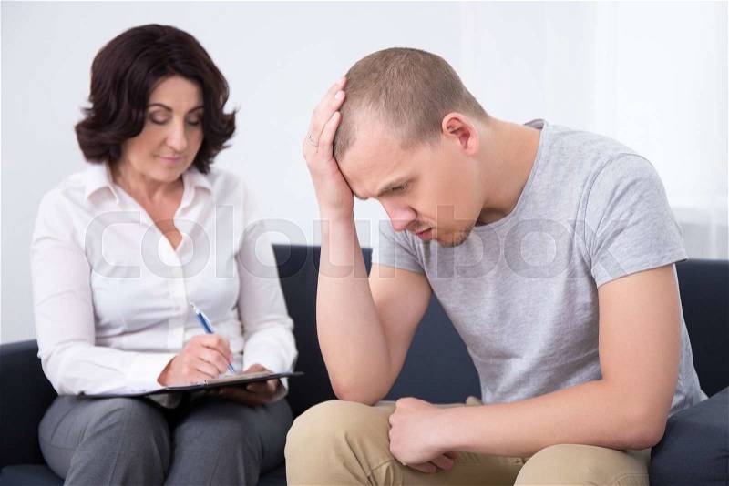 Young sad man talking with psychotherapist or psychologist, stock photo