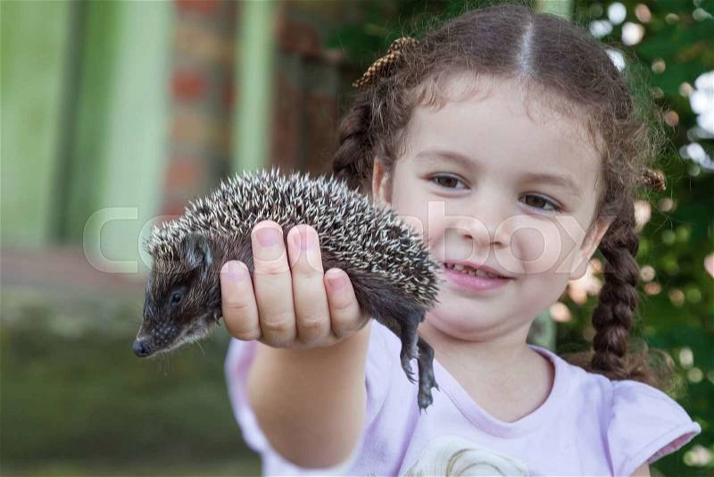 Pretty baby girl holding in his hand young hedgehog outdoors closeup, stock photo