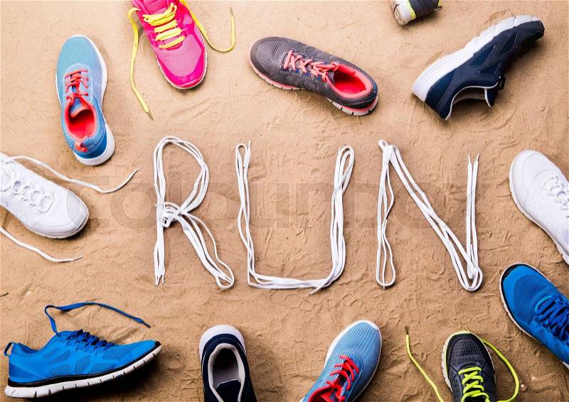 Various colorful running shoes and run sign made of shoelaces against sand background, studio shot, flat lay, stock photo