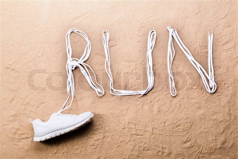 White running shoe and run sign made of shoelaces against sand background, studio shot, flat lay, stock photo