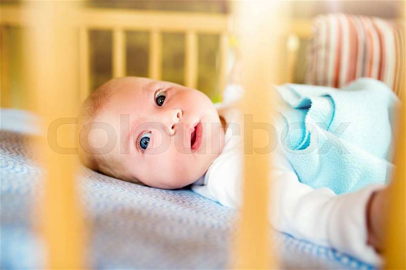 Close up cute little baby boy lying in wooden crib, stock photo