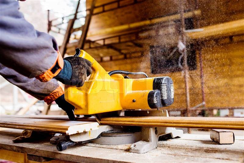 Hands of unrecognizable carpenter working. Man using circular saw to cut planks of wood for home construction, stock photo