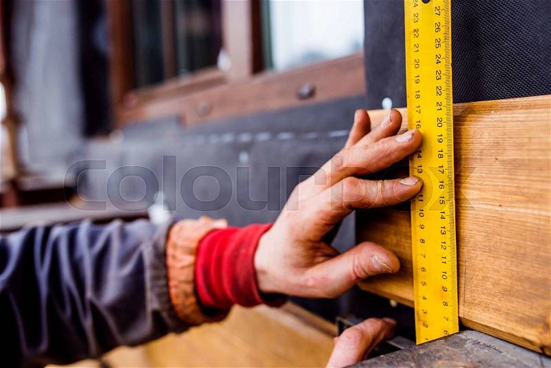 Hands of unrecognizable construction worker thermally insulating house, doing wooden facade, measuring board with yellow tape measure, stock photo