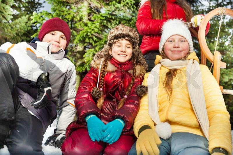 Close up picture of group of friends, boy and girls sitting together outside in snow at the forest, stock photo