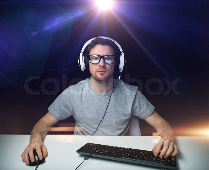 Technology, gaming, entertainment, let\'s play and people concept - young man in headset and eyeglasses with pc computer playing game and streaming playthrough or walkthrough video over light, stock photo