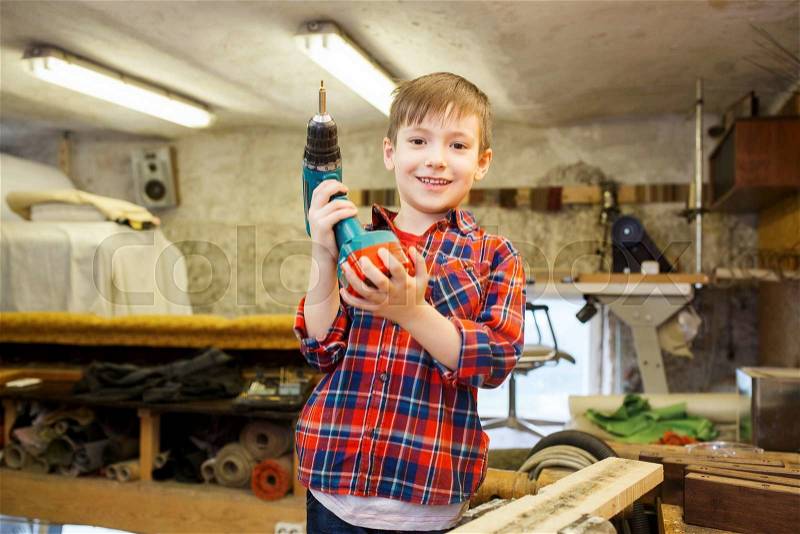 Children, carpentry, profession and people concept - happy little boy with drill at workshop, stock photo