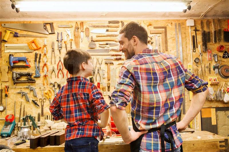 Family, carpentry, woodwork and people concept - happy father and little son working with work tools and wood planks at workshop, stock photo