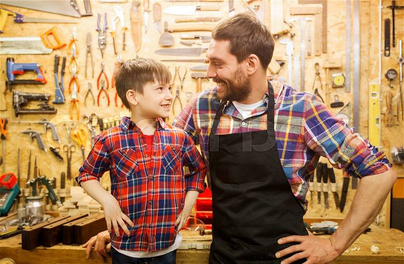 Family, carpentry, woodwork and people concept - happy father and little son working with work tools and wood planks at workshop, stock photo