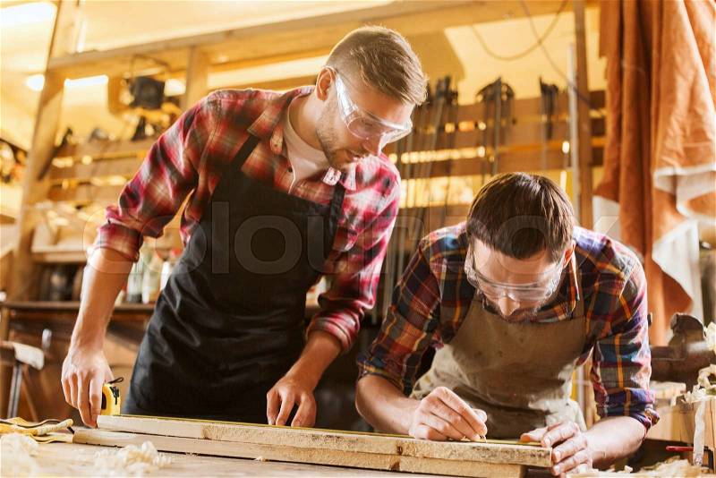 Profession, carpentry, woodwork and people concept - two carpenters with ruler measuring wood plank at workshop, stock photo