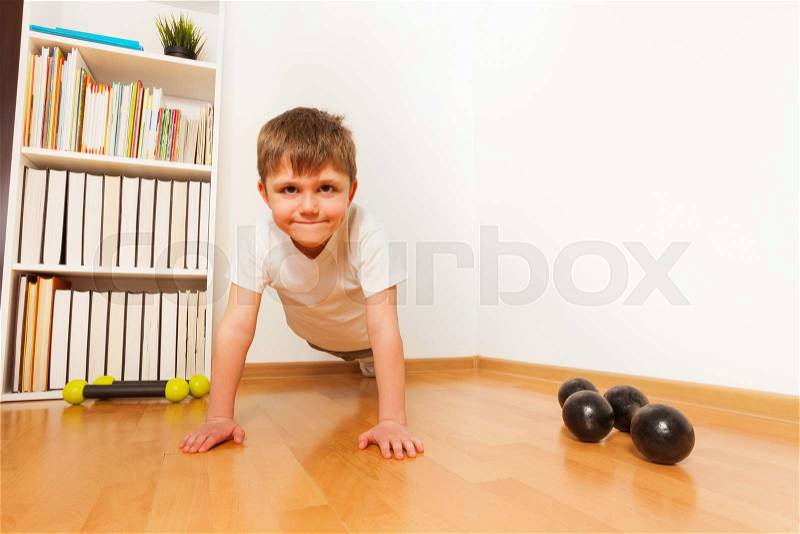 Push-ups or press-ups exercises by preschooler boy working out on the floor, strength training against a white wall with copyspace, stock photo