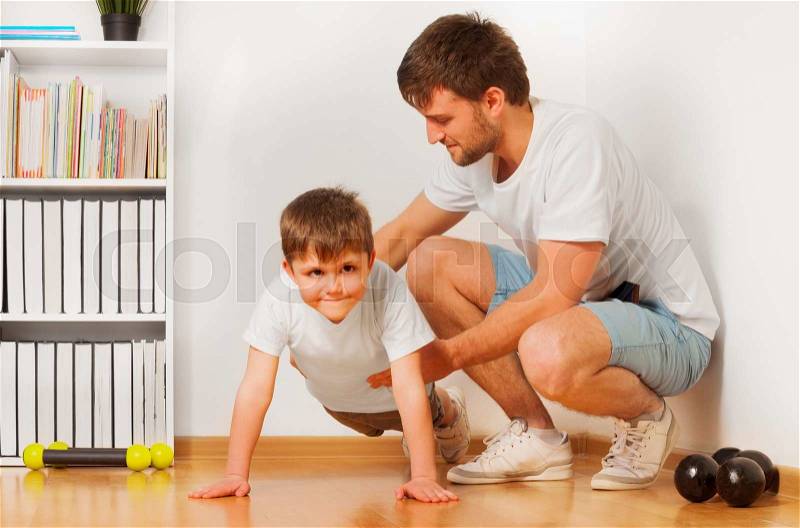 Father teaching his kid son doing exercises, pushing ups or pressing ups at the room, stock photo
