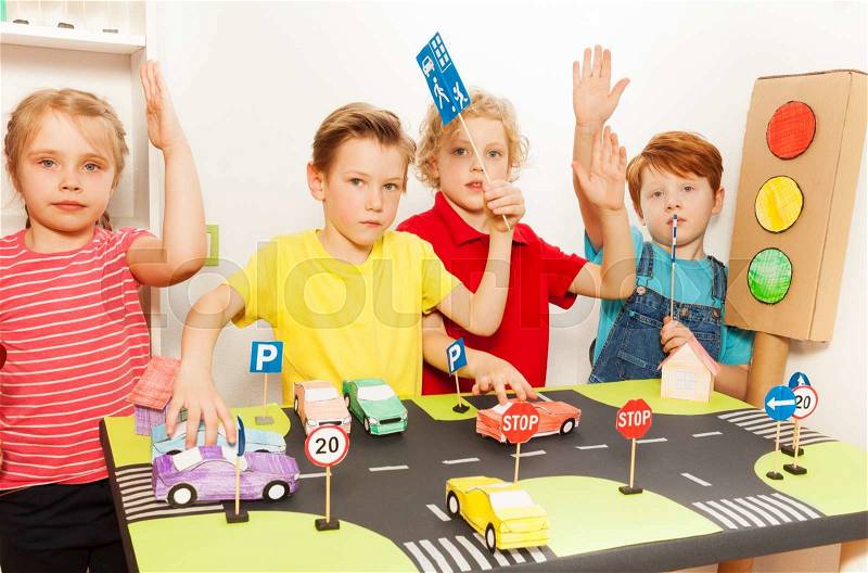 Group of four happy children all raising their hands in the air to answer a question at the road safety lesson, stock photo