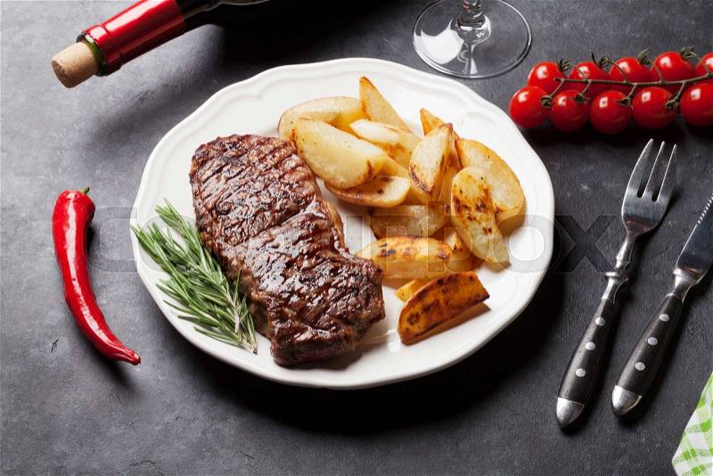 Grilled striploin steak with potato and red wine over stone table, stock photo