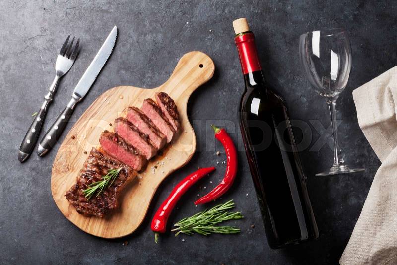 Grilled striploin sliced steak and red wine over stone table. Top view, stock photo