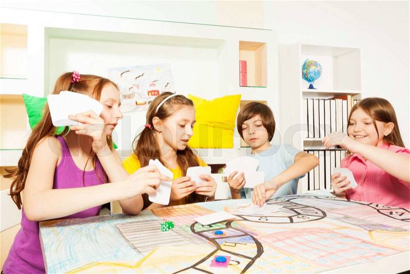 Four friends, ten years old kids, sitting at the table, playing the tabletop game with cards, stock photo