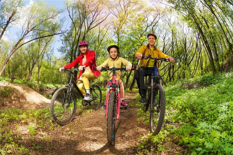 Happy active family, mother, father and girl, mountain biking on forest trail at the sunny day, stock photo
